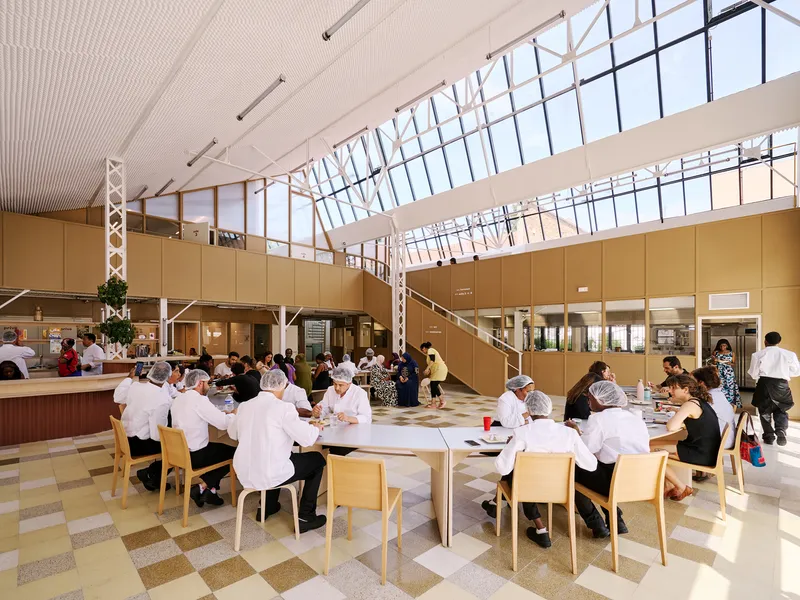Double-height dining hall with saw-tooth clerestory glazing and a raised mezzanine with timber railings