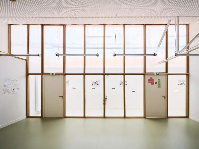 Interior view of timber-framed partition wall with white doors and transom glazing above green flooring