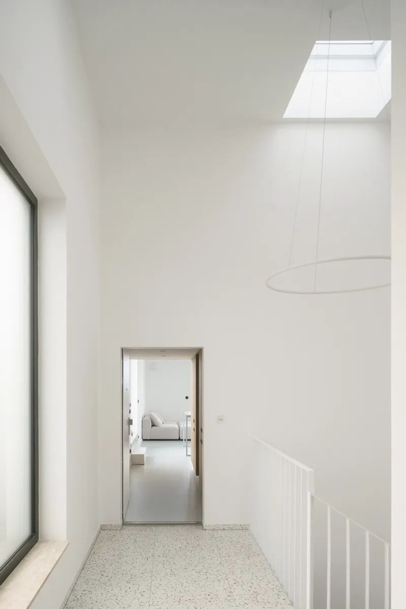 Double-height corridor with terrazzo floor and skylight above a doorway to adjoining rooms