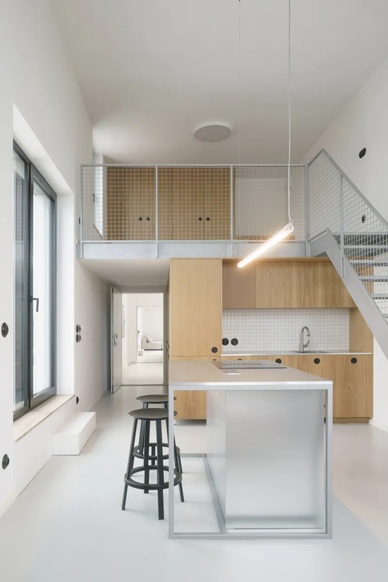 Kitchen with light oak cabinetry and mezzanine with metal mesh balustrade under a sloped ceiling