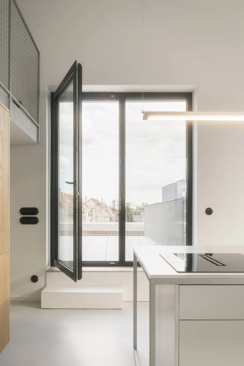 Open glass door from kitchen counter to terrace with neighboring rooflines in view