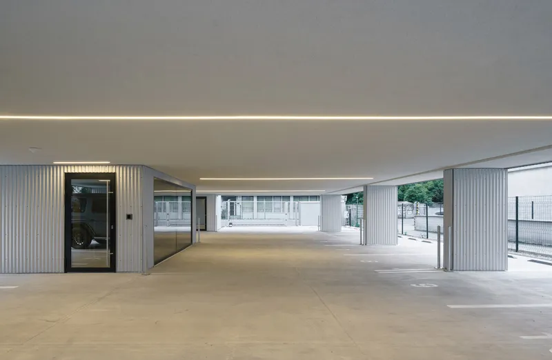 Covered carport with corrugated metal cladding and continuous ceiling slot lighting at dusk