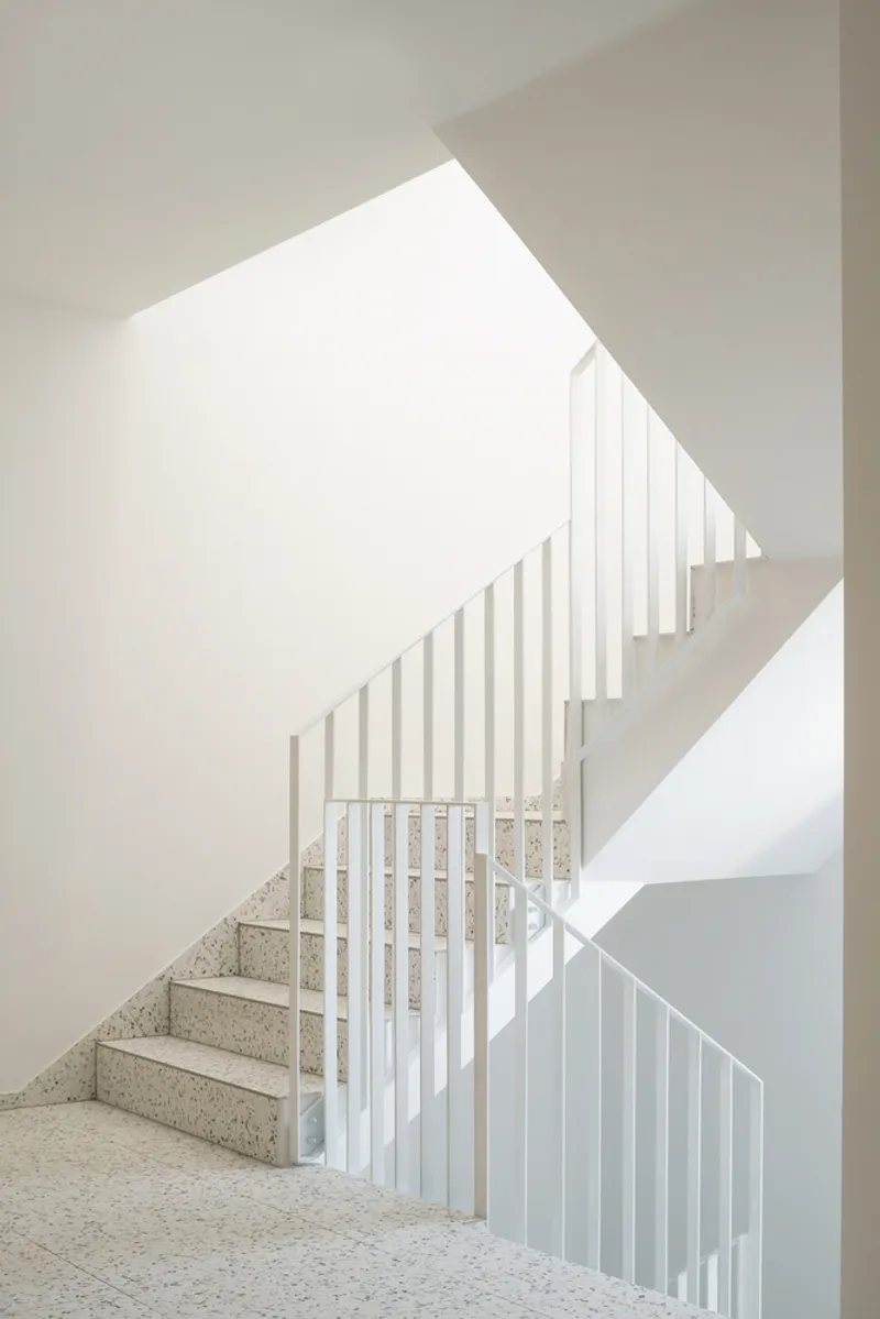 Interior stairwell with terrazzo steps and white vertical slat balustrades under a slanted skylight