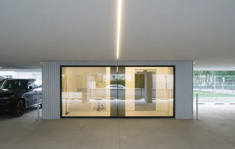 Glass-walled lobby entrance framed by vertical corrugated metal panels beneath the covered parking area