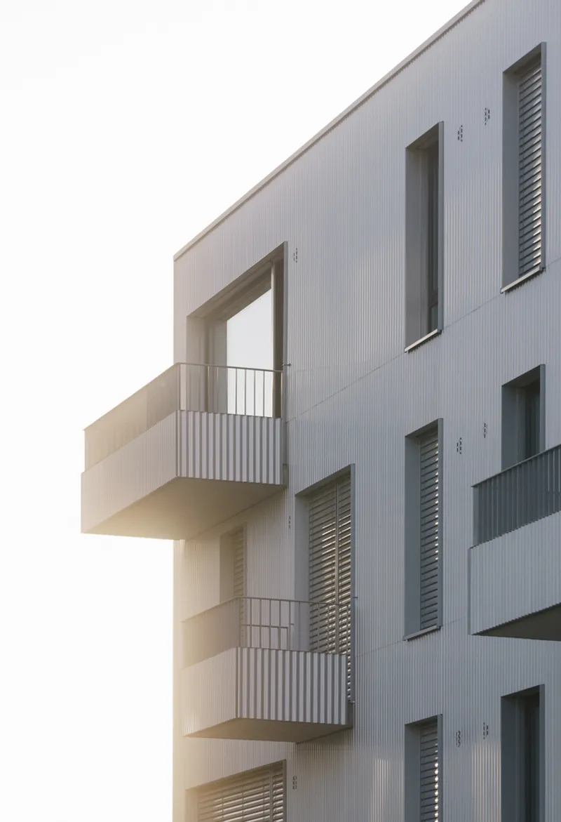 Cantilevered balconies with vertical corrugated metal cladding and louvered shutters under an overcast sky
