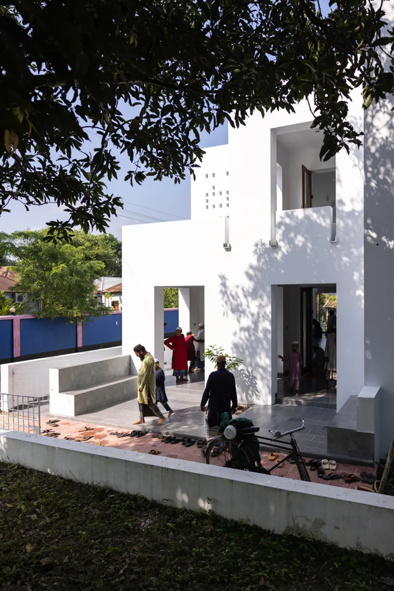 Street view of the white facade with perforations and residents gathering on the raised entrance plinth