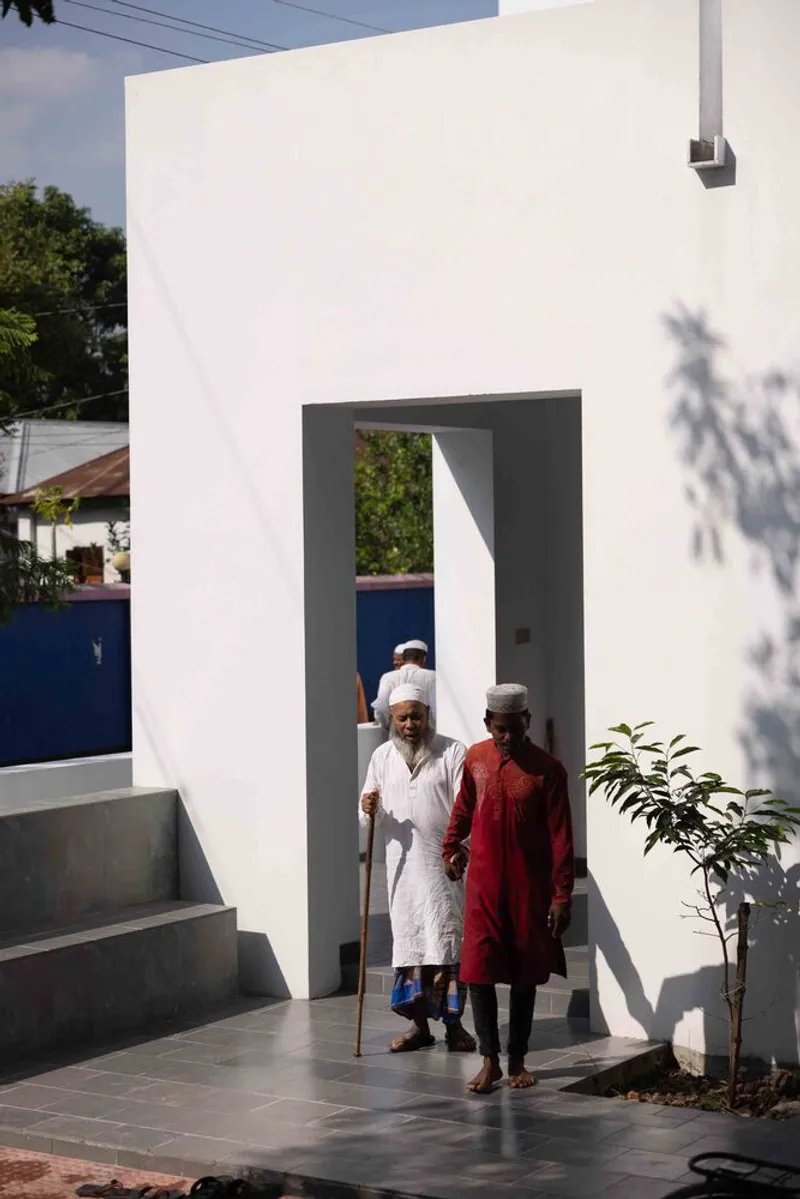 Two figures on an exterior staircase beside a white entry portal casting tree shadows