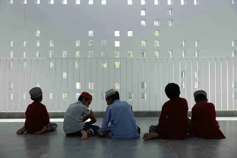 Five people seated on the floor facing a perforated white screen wall filtering sunlight