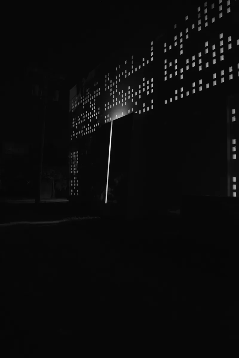 Perforated facade with illuminated rectangular openings forming a pattern at night