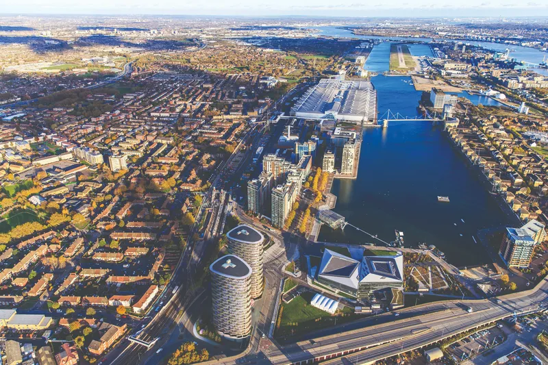 Aerial view of the waterfront development with curved towers beside docks and a cable-stayed bridge