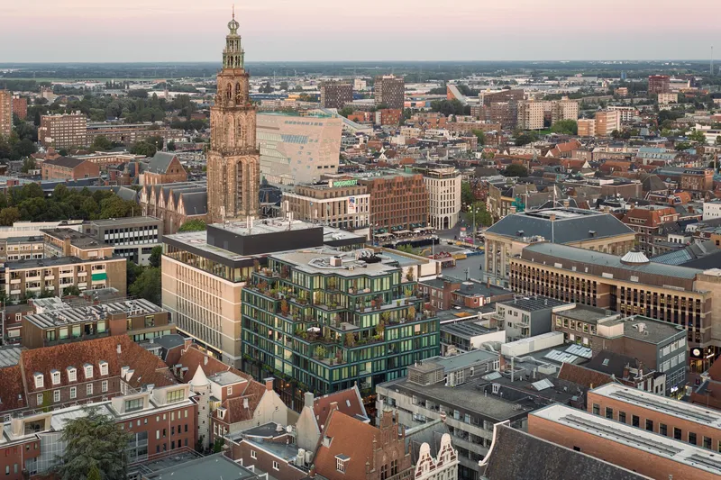 Aerial view of the green glass facade rising above dense historic rooftops at dusk