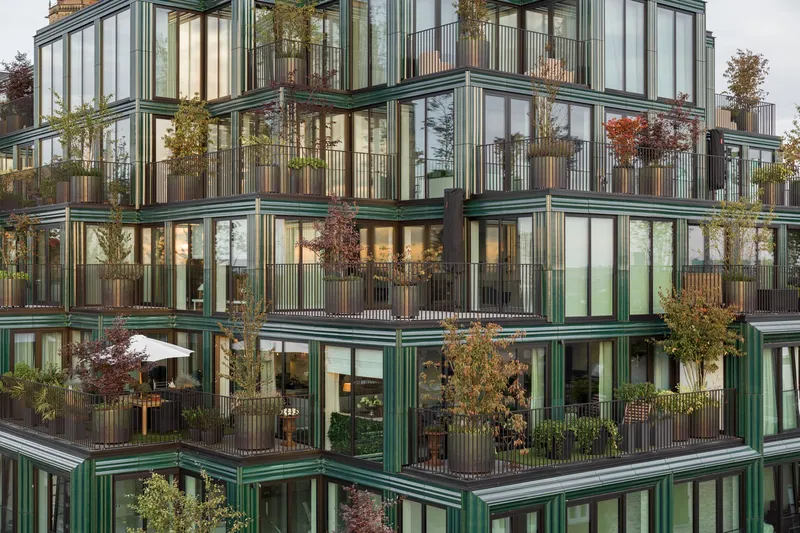 Corner detail of green metal window frames and planted balconies with autumn foliage