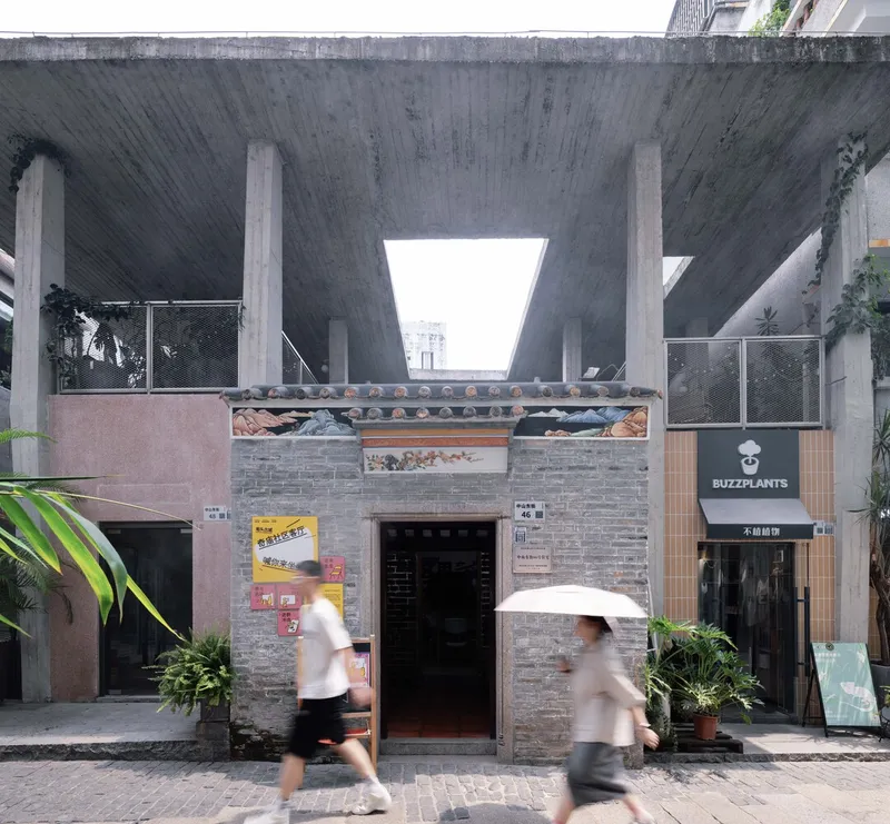 Grey brick storefront with decorative tile band beneath a cantilevered concrete structure as pedestrians pass by