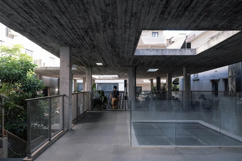 Covered terrace with exposed board-formed concrete ceiling, concrete columns, and glass-walled room flanked by planted terraces