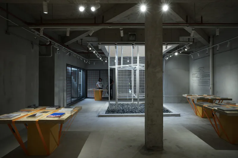 Interior gallery space with exposed concrete columns, track lighting, and central courtyard filled with white gravel