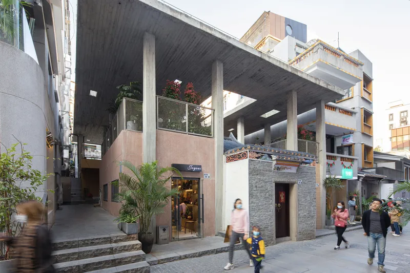 Courtyard view showing mixed-material storefronts sheltered under a concrete frame with potted plants and pedestrians