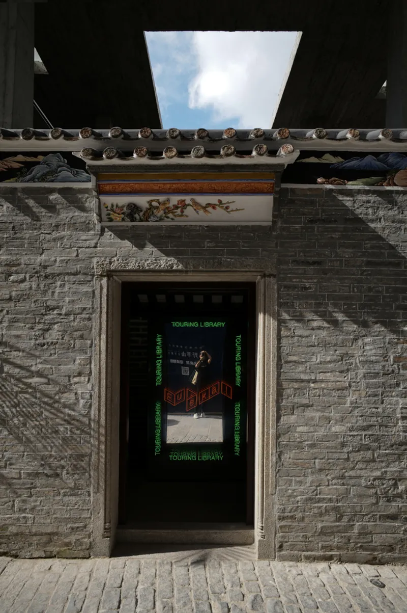 Grey brick entrance wall with decorative tile lintel and rectangular skylight opening framing clouds above
