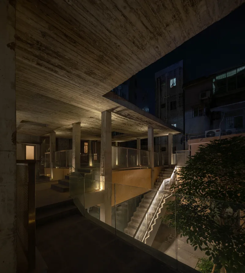 Night view of the illuminated concrete overhang with columns sheltering terraces and a central staircase