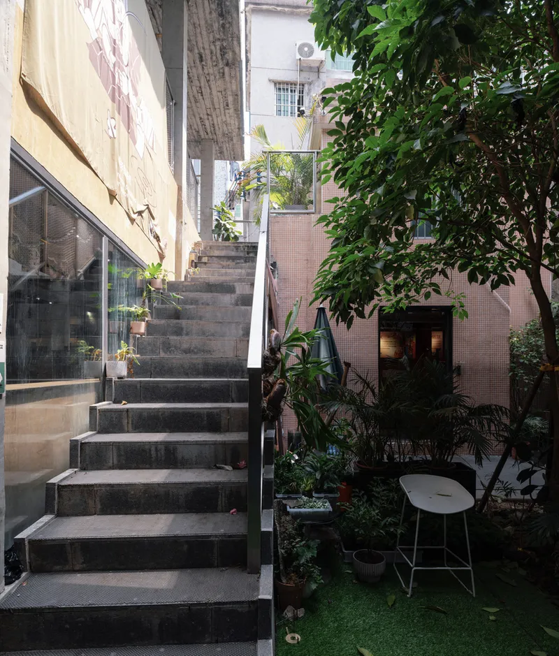 Exterior staircase ascending between glass walls and a planted courtyard with a tree and seating