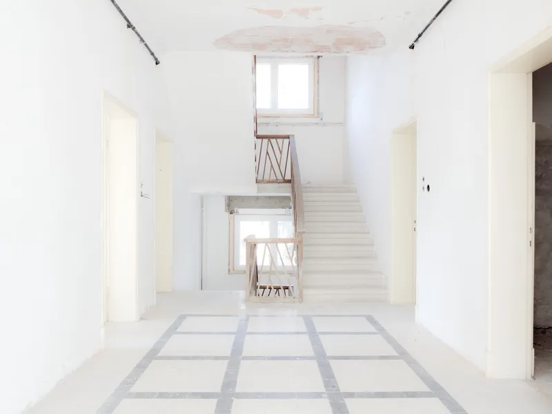 White staircase ascending through a triple-height space with gridded terrazzo floor and exposed timber guardrails