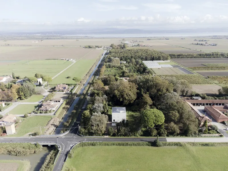 Aerial view of the white cubic volume surrounded by dense tree canopy and agricultural fields
