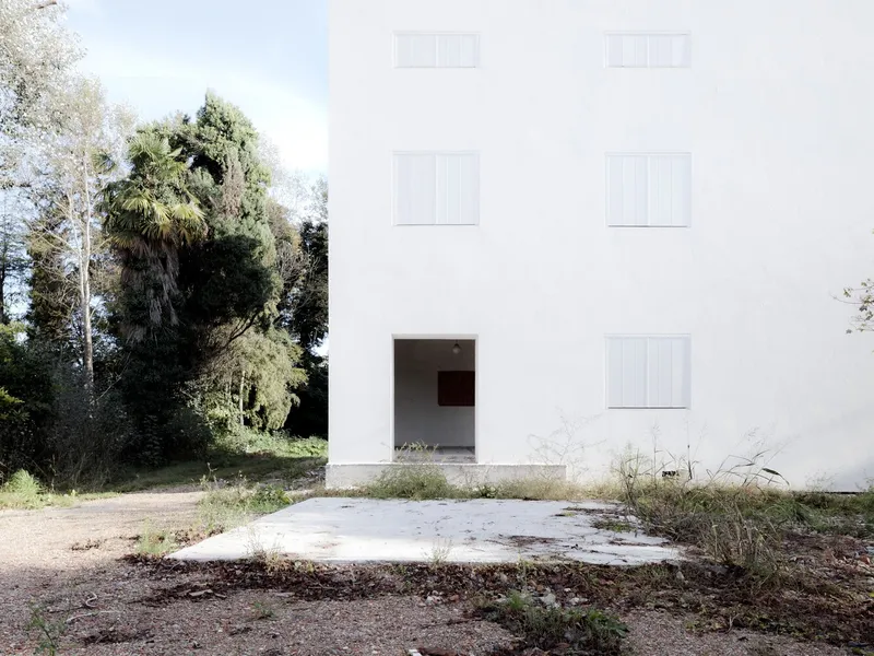 Entrance facade with central opening and recessed shuttered windows on a weathered concrete apron