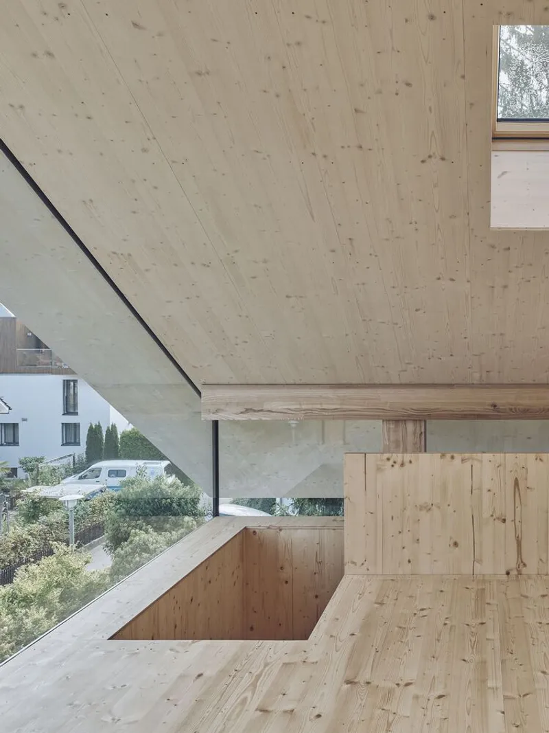 Pale timber interior with horizontal ribbon window overlooking residential buildings and greenery