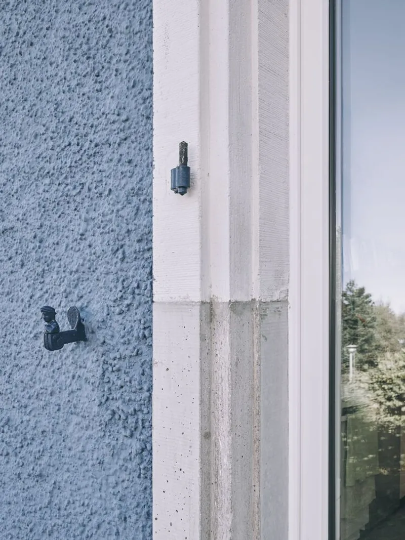 Close-up of window jamb detail showing textured stucco meeting concrete and glazing with fasteners