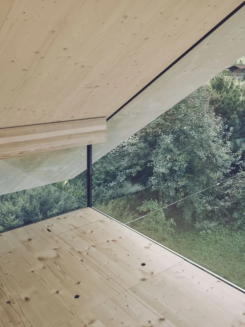 Corner window detail with laminated timber ceiling extending over glass toward sloped garden beyond