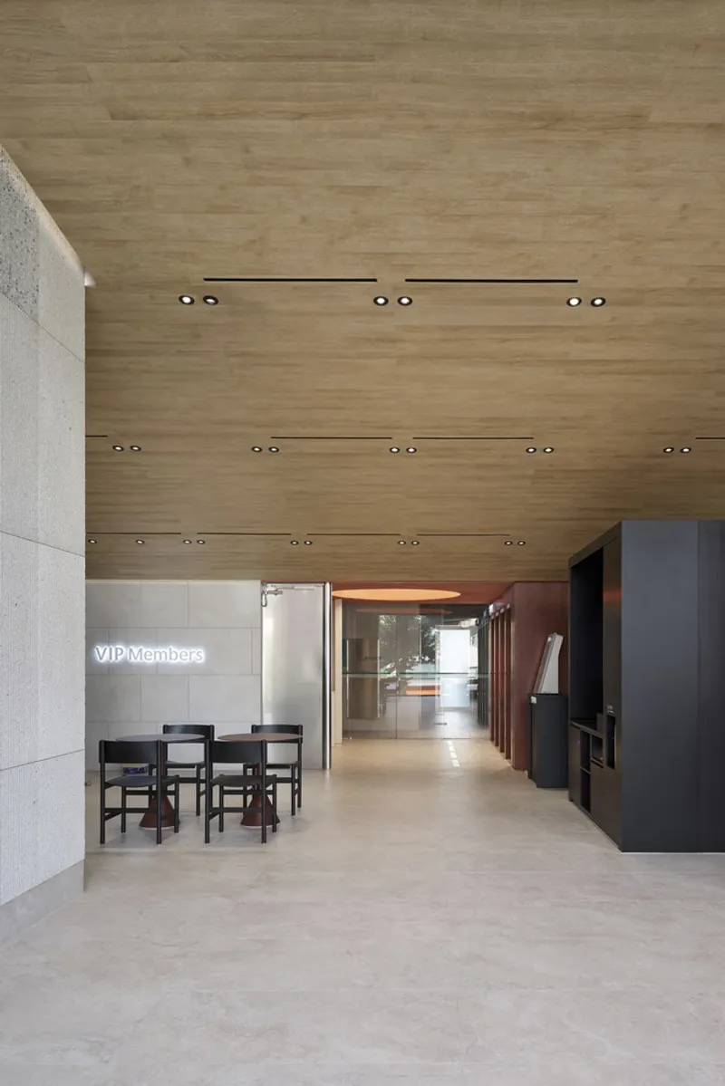 Interior corridor with timber ceiling, recessed downlights, and concrete flooring leading to a distant glazed opening