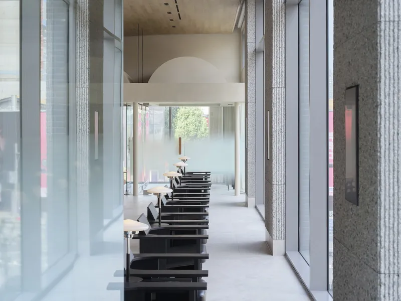 Corridor with textured concrete columns flanking black shelving units and floor-to-ceiling glazing
