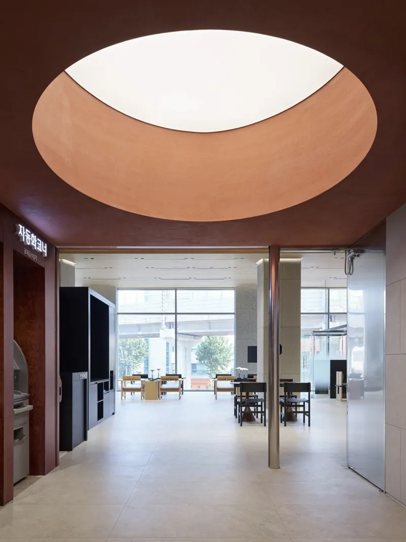 Entrance lobby with circular ceiling opening lined in wood veneer and polished stone flooring