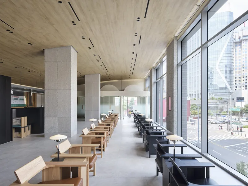 Interior waiting area with rows of timber and black seating along a glazed facade overlooking the street