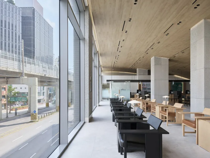 Full-height glazed wall alongside a row of black benches with timber furniture beyond