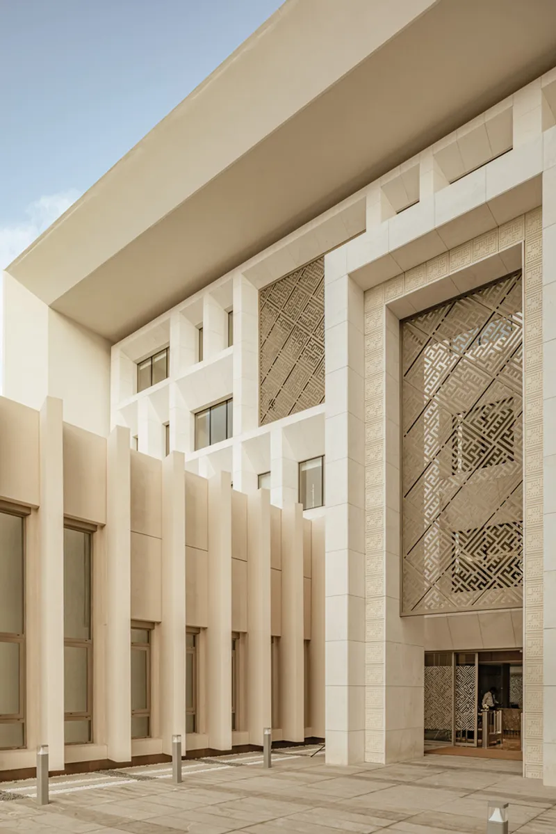 Covered entrance courtyard with vertical stone fins and patterned geometric screen panel under clear skies
