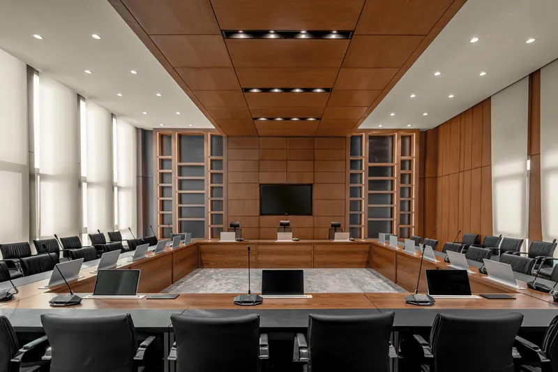 Timber-paneled council chamber with U-shaped seating arrangement and integrated ceiling downlights