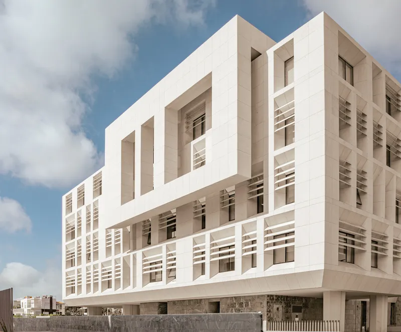 Layered stone facade with recessed windows and deep horizontal banding against scattered clouds