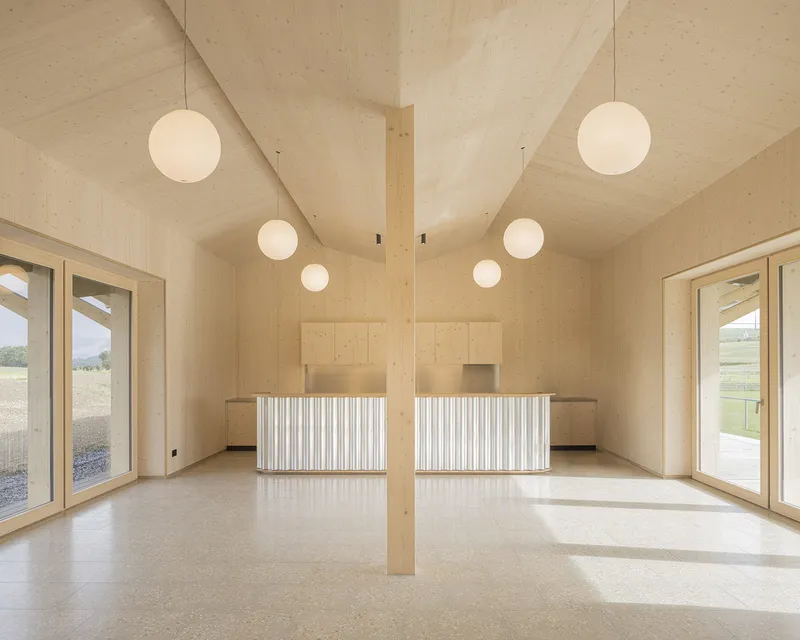 Interior of timber hall with central column, sphere pendant lights and fluted counter units beneath a vaulted ceiling