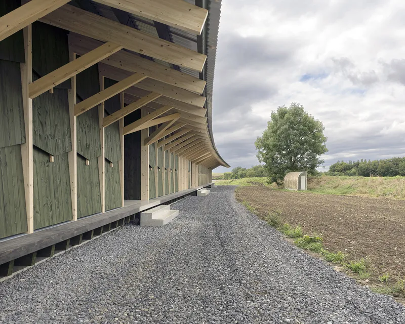 Timber-framed porch with green vertical cladding along a gravel path under an overcast sky