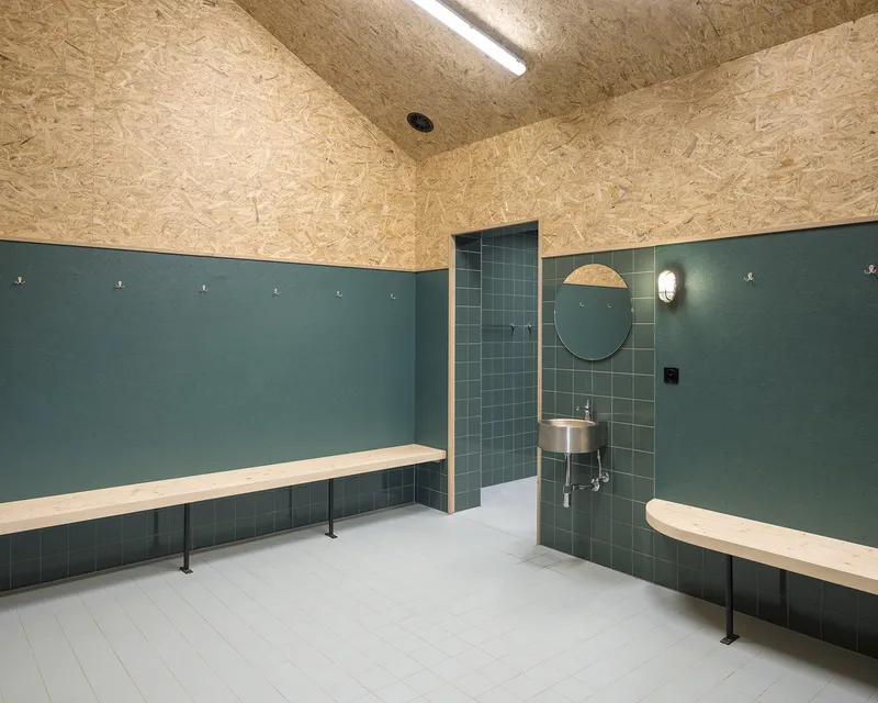 Changing room interior with dark green tile wainscot, OSB ceiling, and pale timber benches