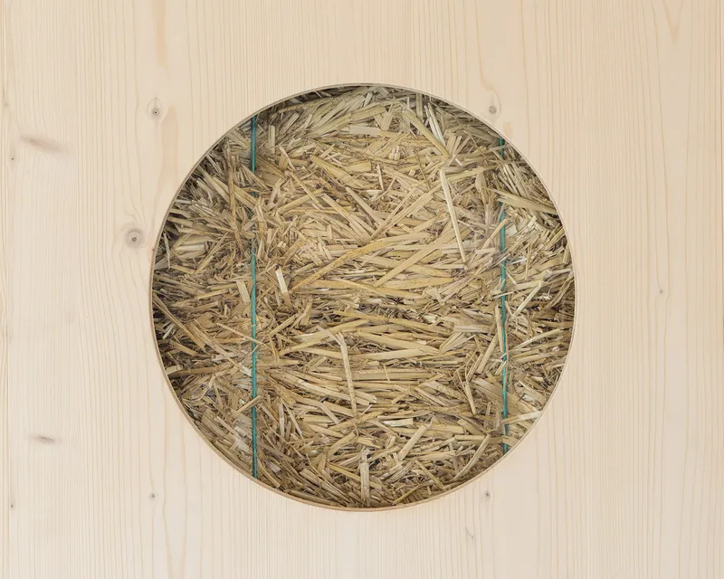 Circular opening in a light timber panel filled with straw and reinforced with wire ties