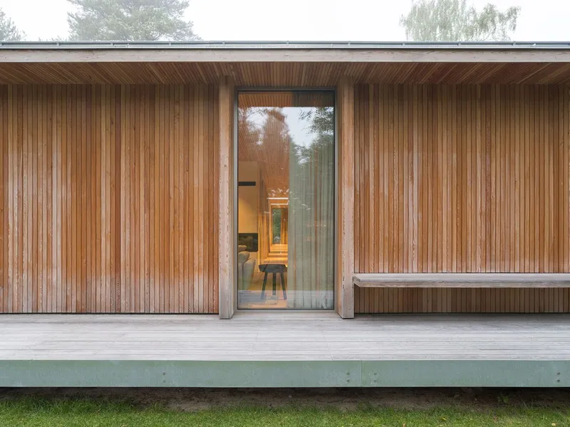 Covered terrace with vertical timber cladding and full-height glazed entry revealing interior in autumn mist
