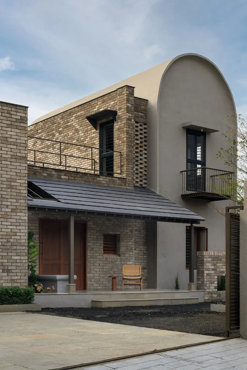 Front elevation combining tan brick and curved plaster volume with metal railings and balconies