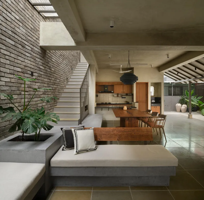 Open-plan living space with brick wall, skylit stairwell and concrete ceiling beams above potted plants