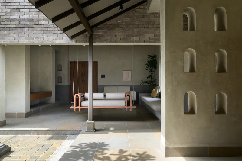Interior courtyard with plastered wall featuring arched niches, exposed timber rafters and dappled sunlight on stone pavers