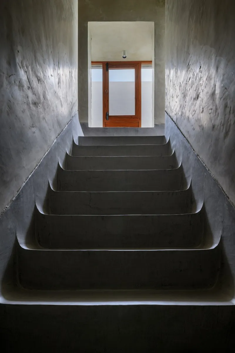 Polished concrete staircase ascending toward timber door framed by textured plaster walls