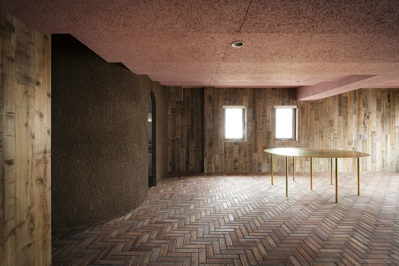 Curved partition wall in dark cork beside herringbone brick floor and brass dining table