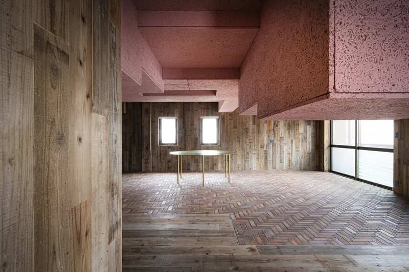Room with brass table centered between timber walls under pink cork ceiling and clerestory windows