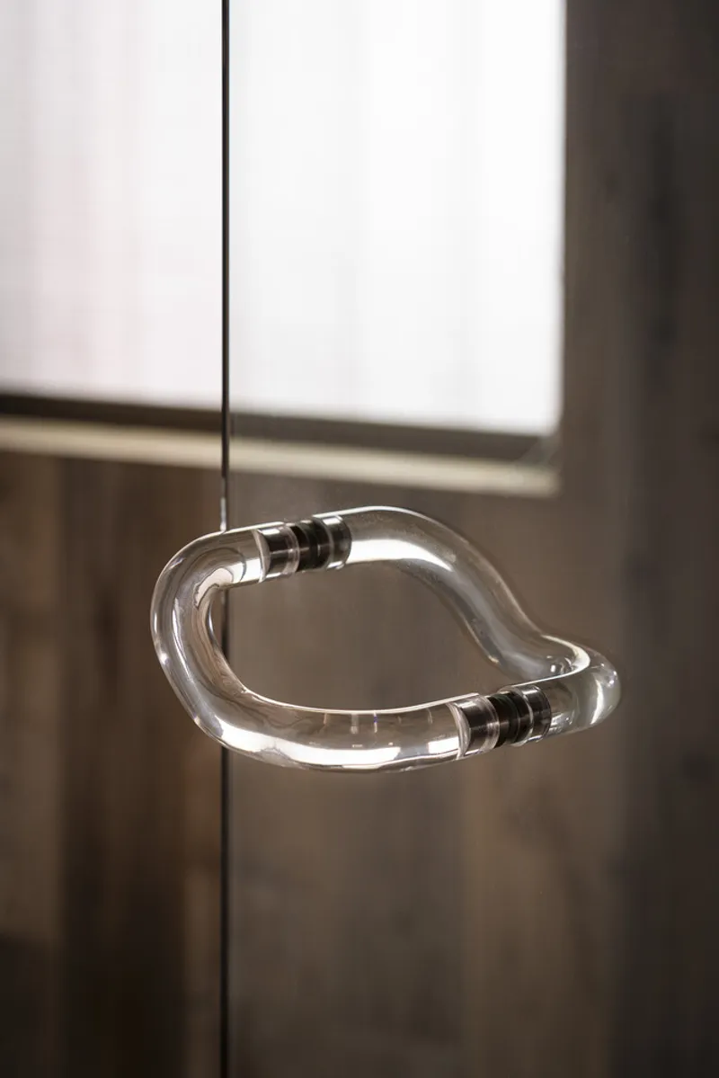 Suspended glass pendant light in an organic curved form illuminated against timber paneling