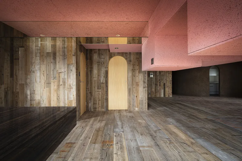 Arched doorway in timber wall beneath pink textured ceiling planes and open floor beyond